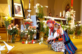 Girls dressed in traditional Polish outfits place flowers in front of a portrait of Pope John Paul II