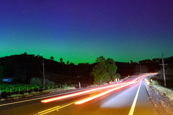 Northern lights or aurora borealis illuminate the night sky along a highway north of San Francisco in Middletown, California