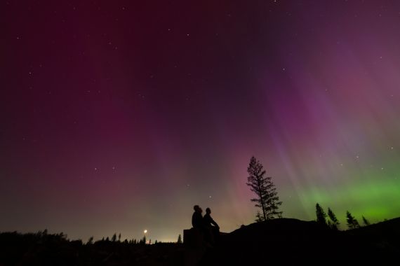 In this image taken with a long exposure, people look at the night sky towards the northern lights, or Aurora Borealis, on Friday, May 10